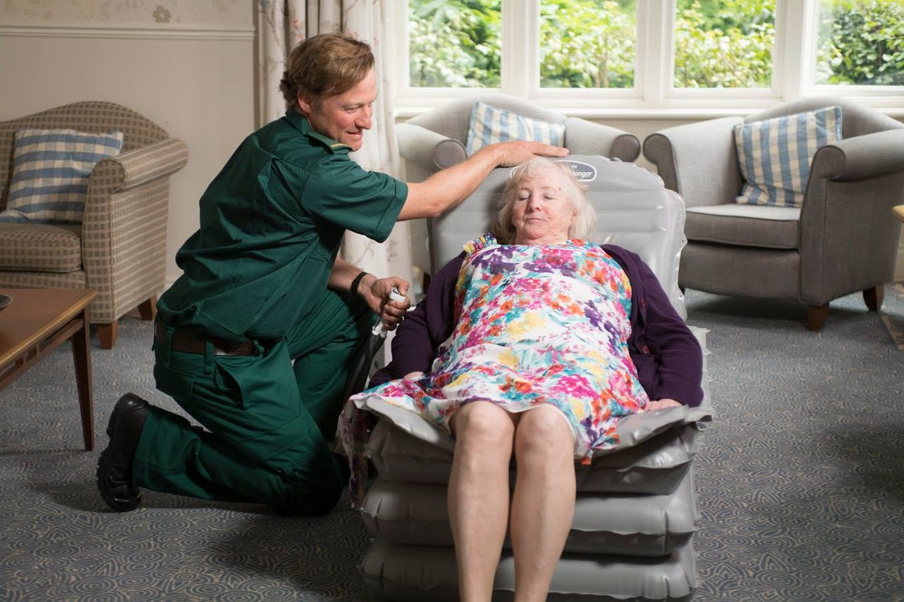 A senior man being safely lifted from the floor in his home by a first responder and a caregiver using an inflated Mangar inflatable lifting cushion.
