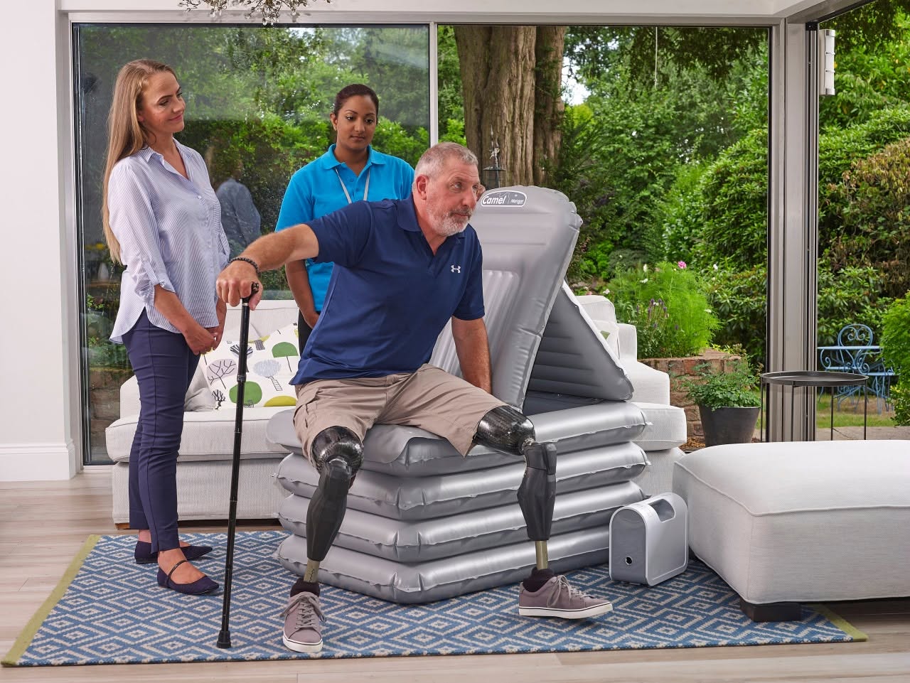 A friendly customer service representative in a mobility equipment showroom, smiling next to displayed in-stock items like a Raizer lifting chair and Mangar lifting cushions, illustrating expert help for home mobility solutions.